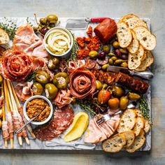 an assortment of meats, bread and olives on a platter with utensils