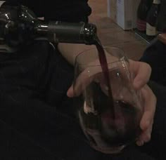 a person holding a wine glass with red wine being poured into it, while another person sits in the background