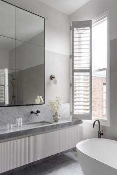 a white bath tub sitting next to a large mirror on the wall in a bathroom