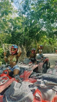 three people on four wheelers in the woods with trees and bushes behind them, one woman is talking on her cell phone