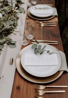 the table is set with gold and white plates, silverware, and greenery