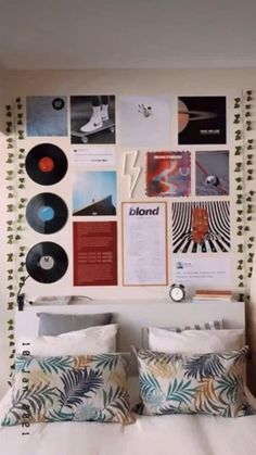 a bed topped with lots of pillows next to a wall covered in pictures and records