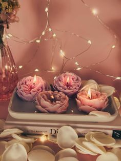 three pink roses sitting on top of a tray next to a vase filled with flowers