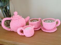 pink crocheted tea set sitting on top of a wooden table