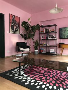 a living room with pink walls, black furniture and a polka dot rug on the floor