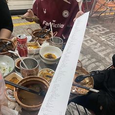 people sitting at a table with food and drinks on it, one person is holding a piece of paper