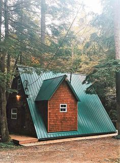 a small cabin in the woods with a metal roof and green tining on it