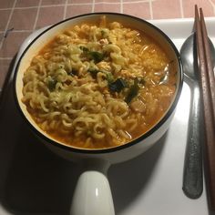 a bowl of soup with chopsticks next to it on a plate, ready to be eaten