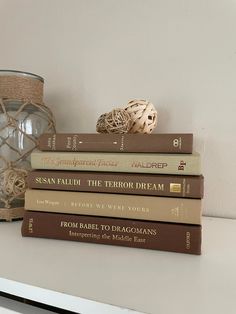 a stack of books sitting on top of a white table next to a glass vase