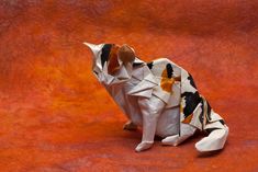 an origami animal made out of paper on a red surface with black and white spots