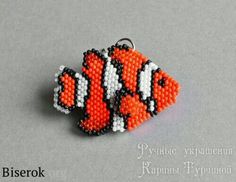 an orange and white fish beaded charm on a gray surface with the words biserok written below it