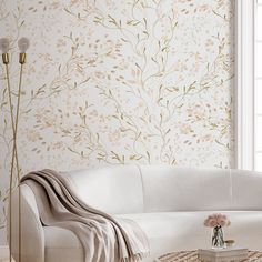 a white couch sitting in front of a window next to a vase with flowers on it