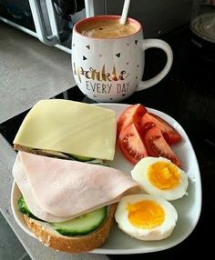 a sandwich with eggs, tomato and cucumber next to a cup of coffee