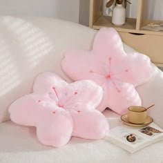 two pink flower pillows sitting on top of a white couch next to a coffee cup