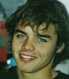 a close up of a person with blue eyes and curly hair smiling at the camera