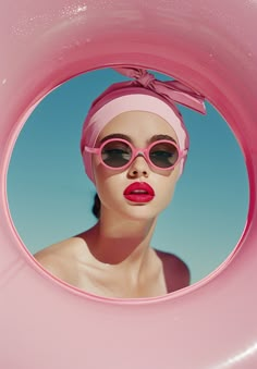 a woman wearing sunglasses and a pink hat is seen through a hole in a pool float