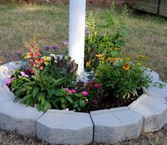 a cement planter with flowers in it on the ground next to a white pole