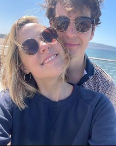 a man and woman taking a selfie in front of the ocean on a sunny day