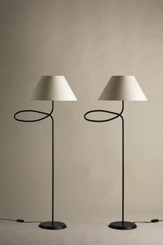 two lamps with white shades on them are standing in front of a gray wall and floor