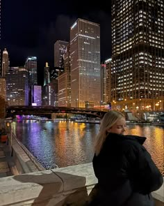 a woman is sitting on a ledge looking at the water and buildings in the background