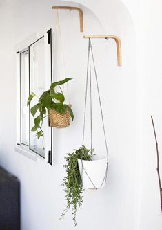 two hanging planters with plants in them on the wall next to a mirror and couch