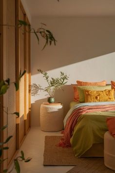 a bed with green and orange pillows in a bedroom next to a potted plant