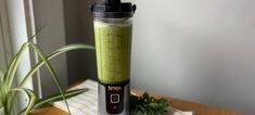 a blender filled with green liquid sitting on top of a table next to a potted plant