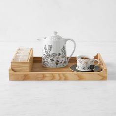 a wooden tray with two cups and a teapot on it, sitting next to each other