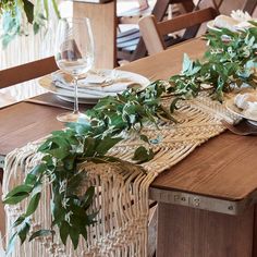 the table is set with place settings and greenery on it, along with wine glasses