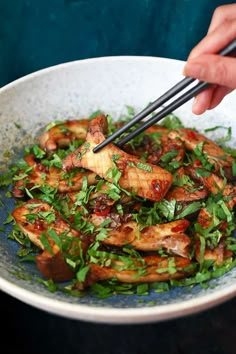 someone holding chopsticks over a bowl of food with greens and meat on it