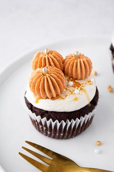 two cupcakes with frosting and gold decorations on a plate next to a fork