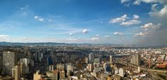 an aerial view of a city with tall buildings and mountains in the distance under a blue sky