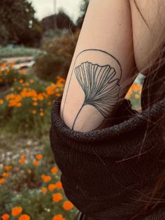 a woman's arm with a tattoo on it and orange flowers in the background