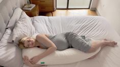 a woman laying on top of a white bed in the middle of a room next to a window