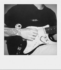 black and white photograph of a man playing an electric guitar with tattoos on his arm