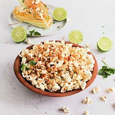 a wooden bowl filled with popcorn next to lime wedges on a white counter top