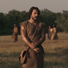 a man standing in the middle of a field with his hands on his hips and other people behind him