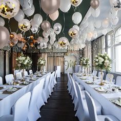 a room filled with lots of tables covered in white tablecloths and balloons hanging from the ceiling