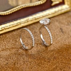 two diamond rings sitting on top of a table next to a framed photo and gold frame