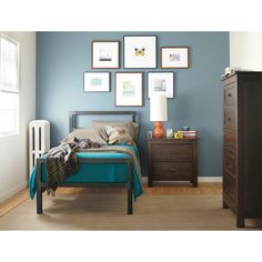 a bedroom with blue walls and pictures on the wall above the bed, along with a chest of drawers