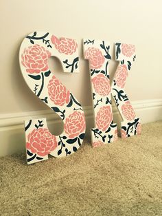 the letters are made out of wood and have pink flowers on them, along with a white wall