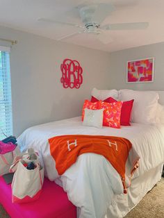 a white bed with orange and pink pillows on top of it next to a window