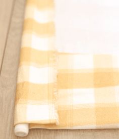 a yellow and white checkered table cloth laying on top of a wooden floor next to a knife