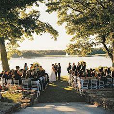 a wedding ceremony on the side of a lake with people sitting in chairs and facing each other