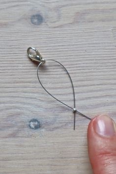 a hand holding a pair of scissors on top of a wooden table next to a piece of wire