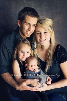 a man, woman and child are posing for a family photo in front of a dark background