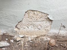 a large rock sitting on the ground next to a cement wall with cracks in it