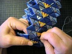 two hands are working on an origami object that is blue and yellow in color