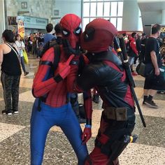 two people dressed as deadpool and spider - man are standing in an airport lobby