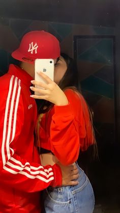 a woman taking a selfie in front of a mirror wearing a red baseball cap